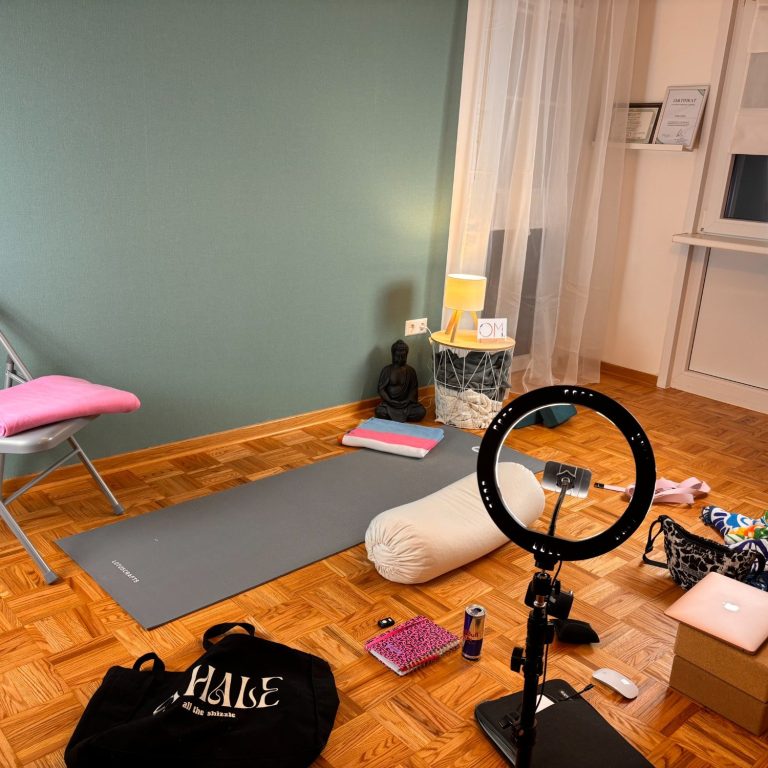 Ein ruhiger Raum mit einer Yogamatte, Kissen, Lehrmaterialien und einem Ringlicht.