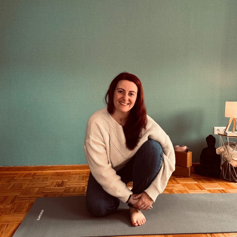 Meike sitzt auf einer Yogamatte in einem hellen Raum.